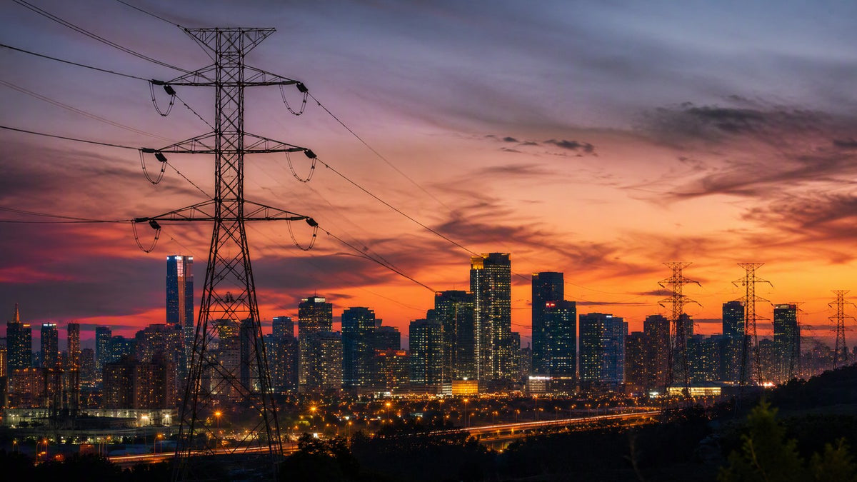 A city skyline at dusk with glowing windows and power transmission lines in the foreground