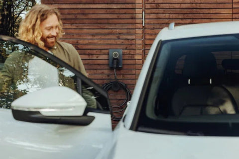 Man next to white electric car by wooden wall with EV charging station