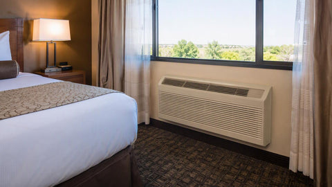 Aire acondicionado PTAC a través de pared instalado en la pared de una habitación de hotel bajo una ventana grande