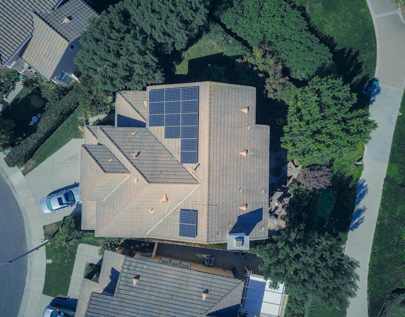 Aerial view of a suburban house with rooftop solar panels and surrounding trees