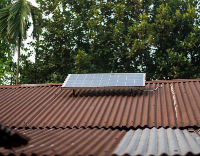 Solar panel installed on a rusty metal roof with green trees in the background.