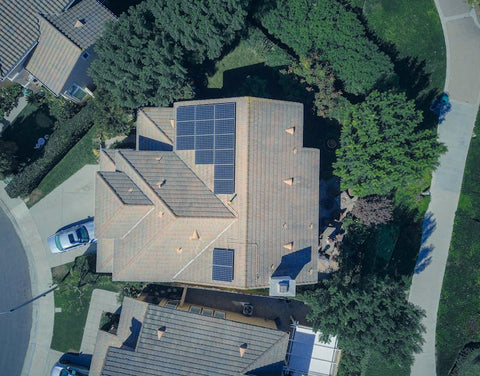 Aerial view of a suburban house with rooftop solar panels and surrounding trees