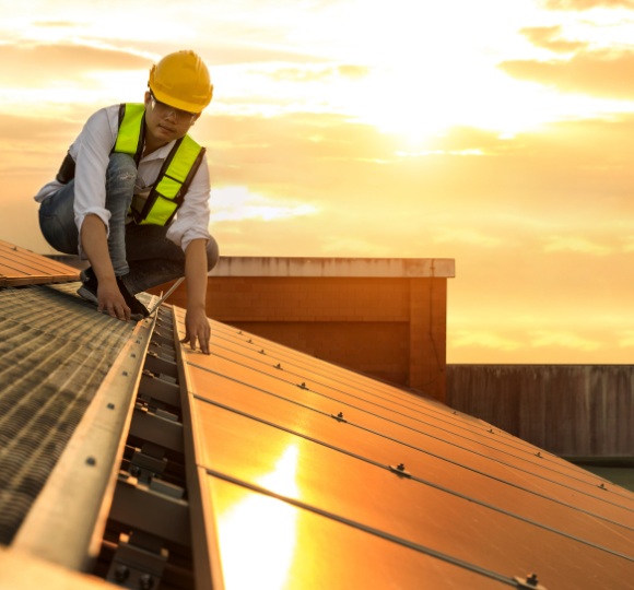 Person installing solar panels on a roof with a sunset background