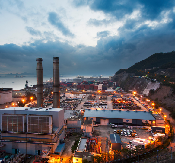 Industrial area with large chimneys and warehouses under a cloudy sky.