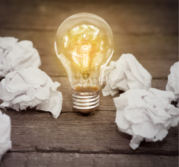 Light bulb with crumpled papers on a wooden surface