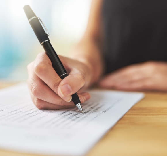 Hand holding a pen writing on a piece of paper with a blurred background