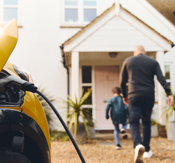 Family walking towards a house with an electric vehicle charging cable in the foreground.