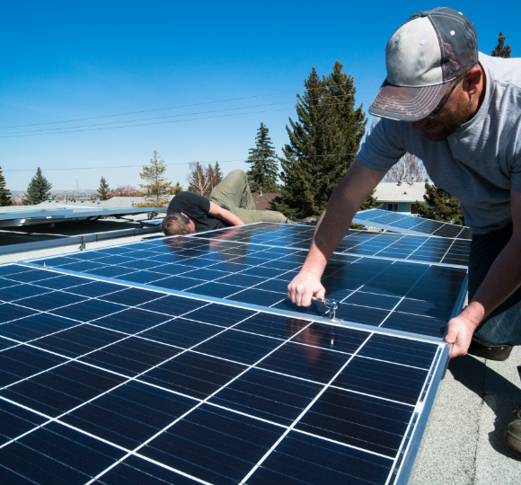 Two people installing solar panels on a roof with clear blue sky